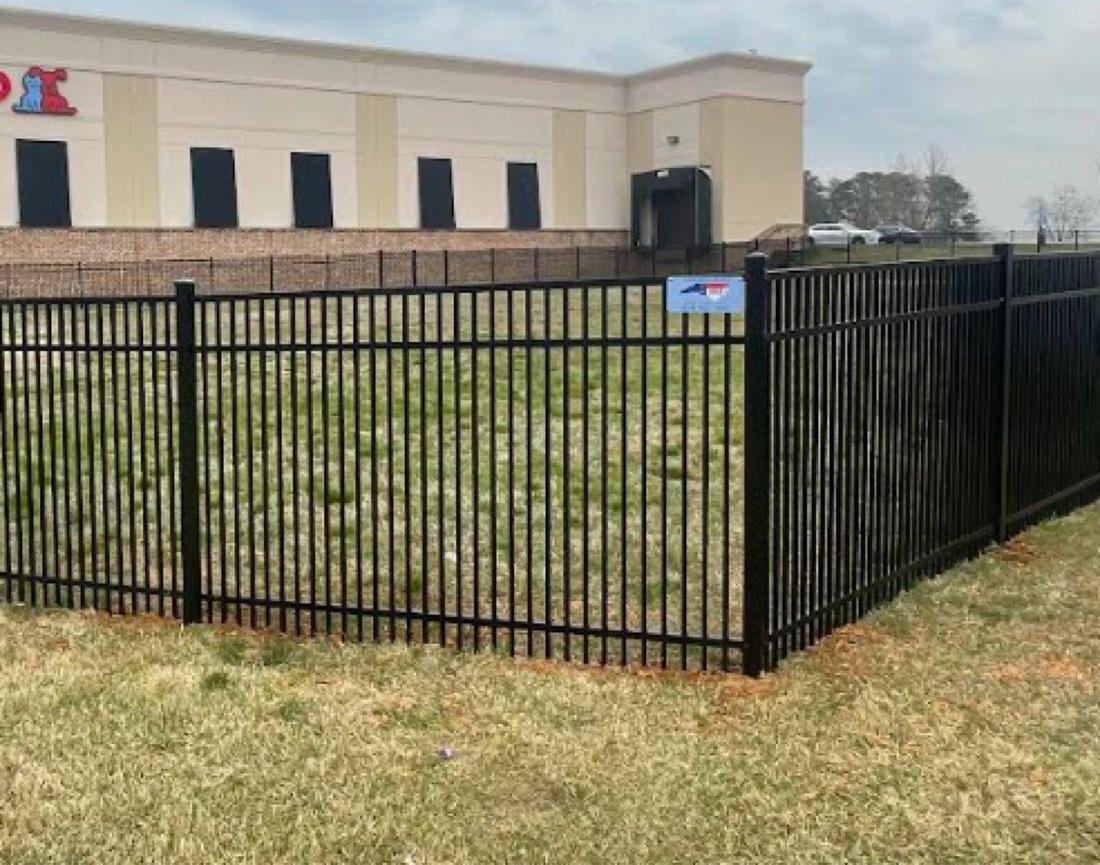 A black aluminum fence running along the lawn of a single-story commercial building.