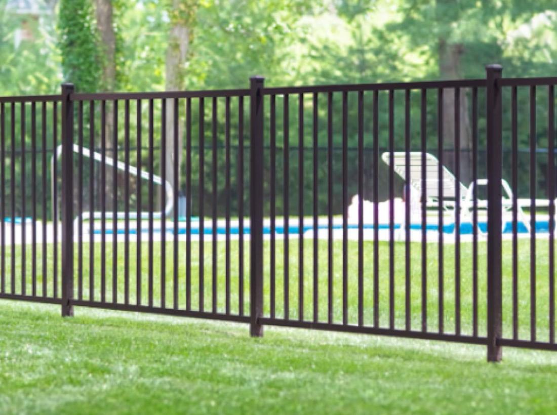 A dark bronze aluminum fence across a lawn with a pool and loungers behind it.