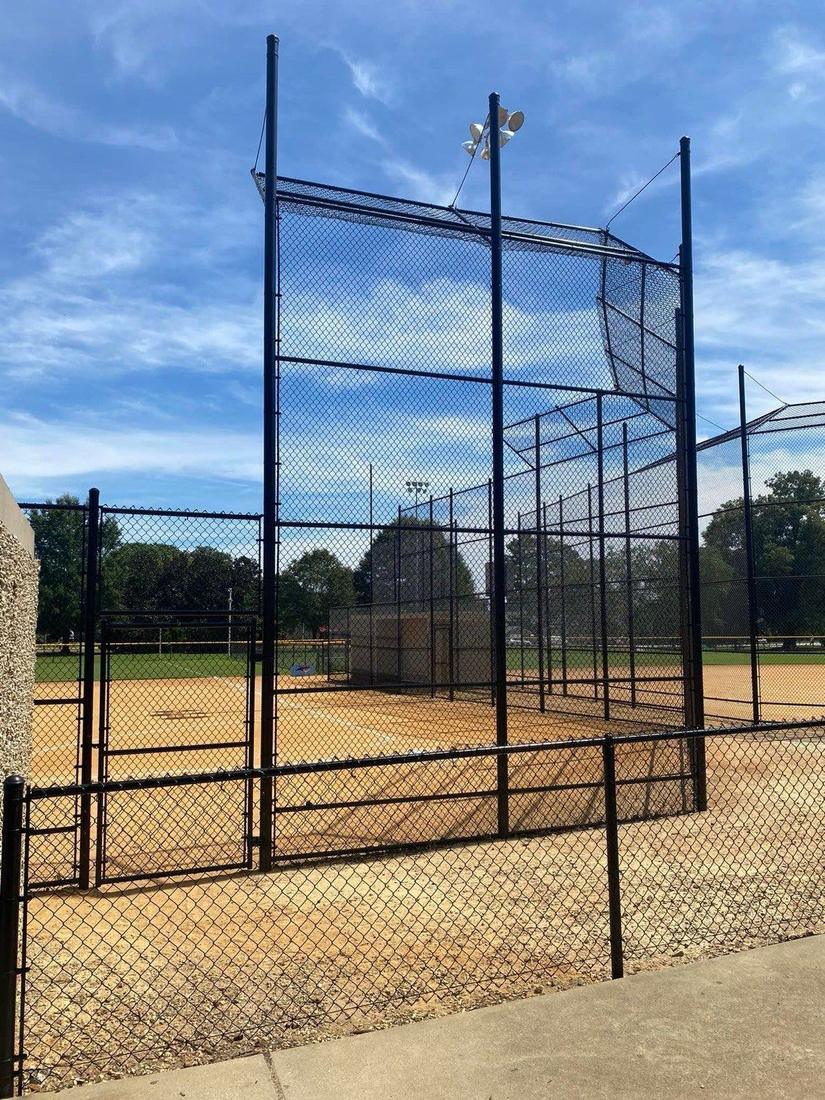 A tall black chain link backstop with overhead netting at a baseball field.