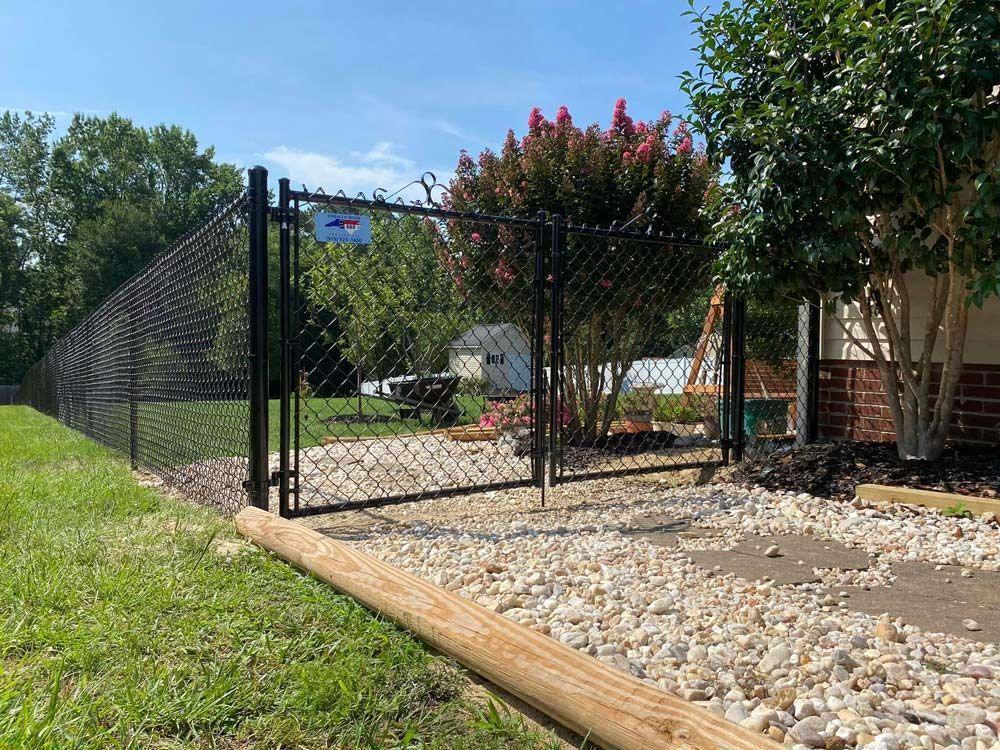 A black chain link fence and gate along a white gravel bed, crepe myrtle above.