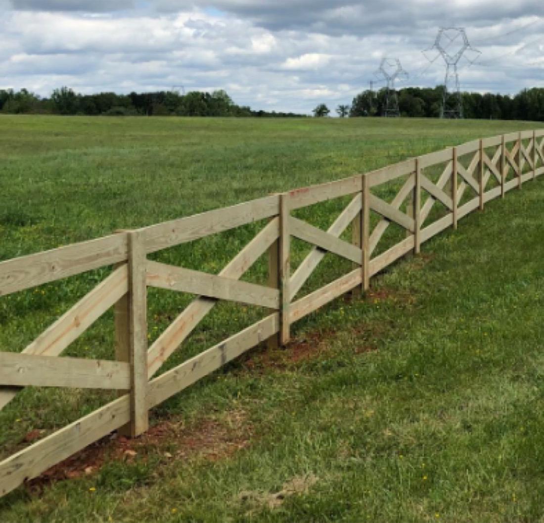 A wood crossbuck fence running across an open field under a cloudy sky.