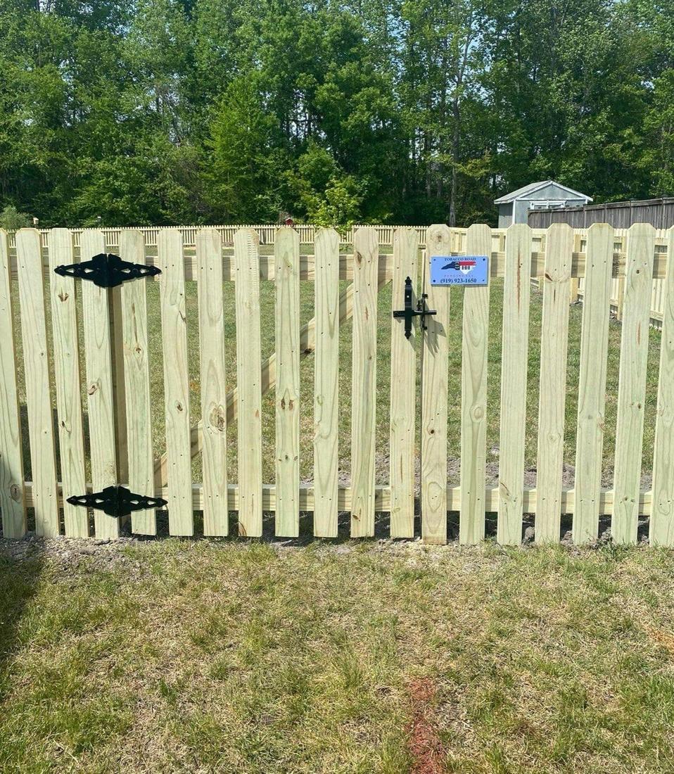A wood shadowbox gate with decorative black strap hinges and latch, set in a matching fence.