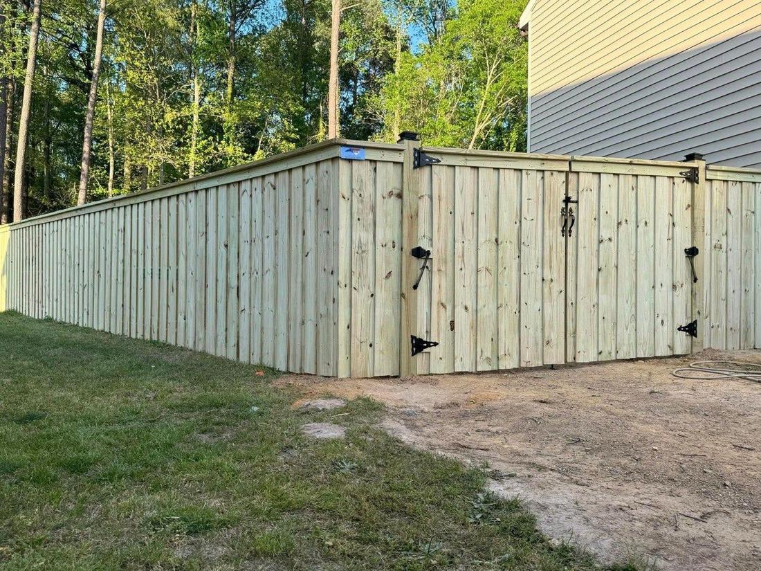 A wood privacy fence turning a corner with a gate in the run, woods and a house behind.