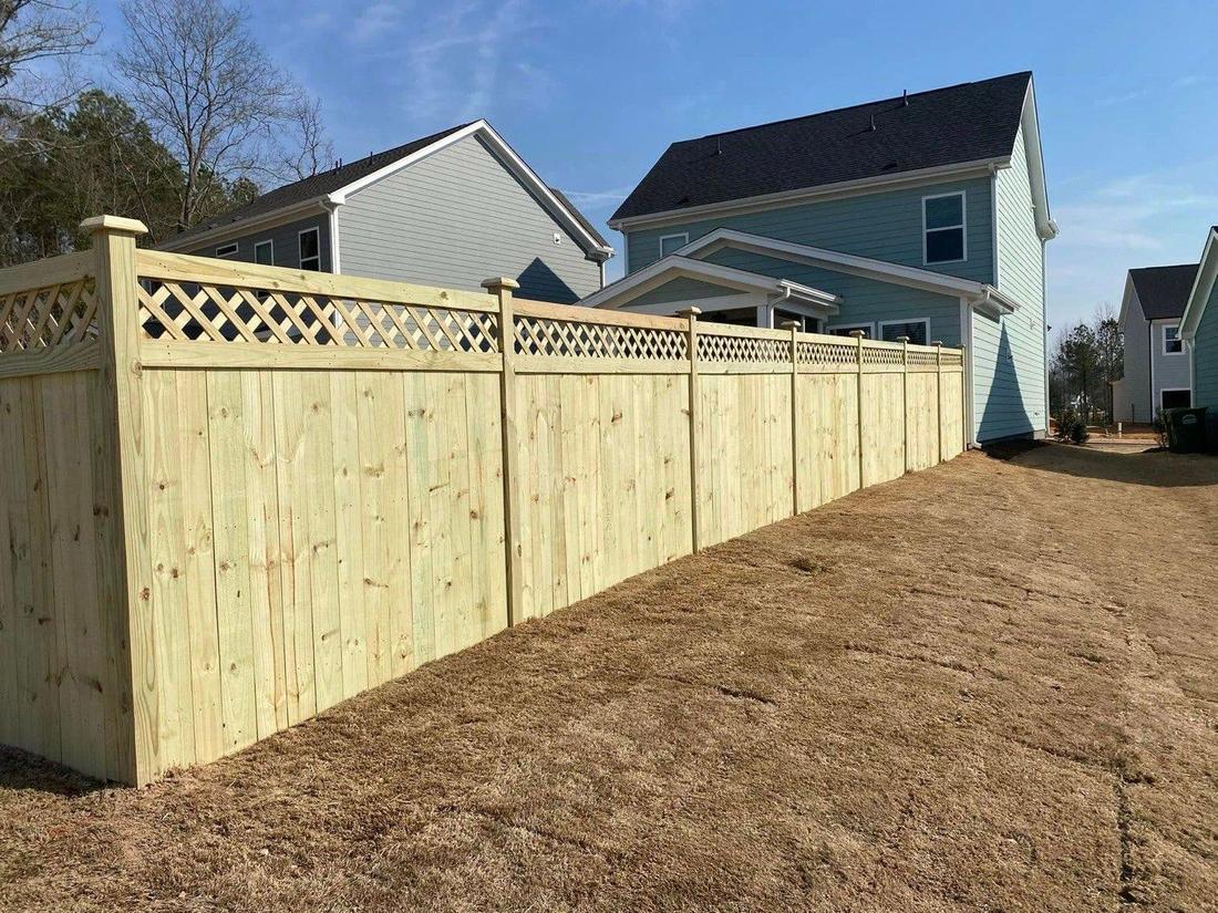 A tall wood privacy fence with a lattice topper running the length of a bare-earth yard, houses behind.