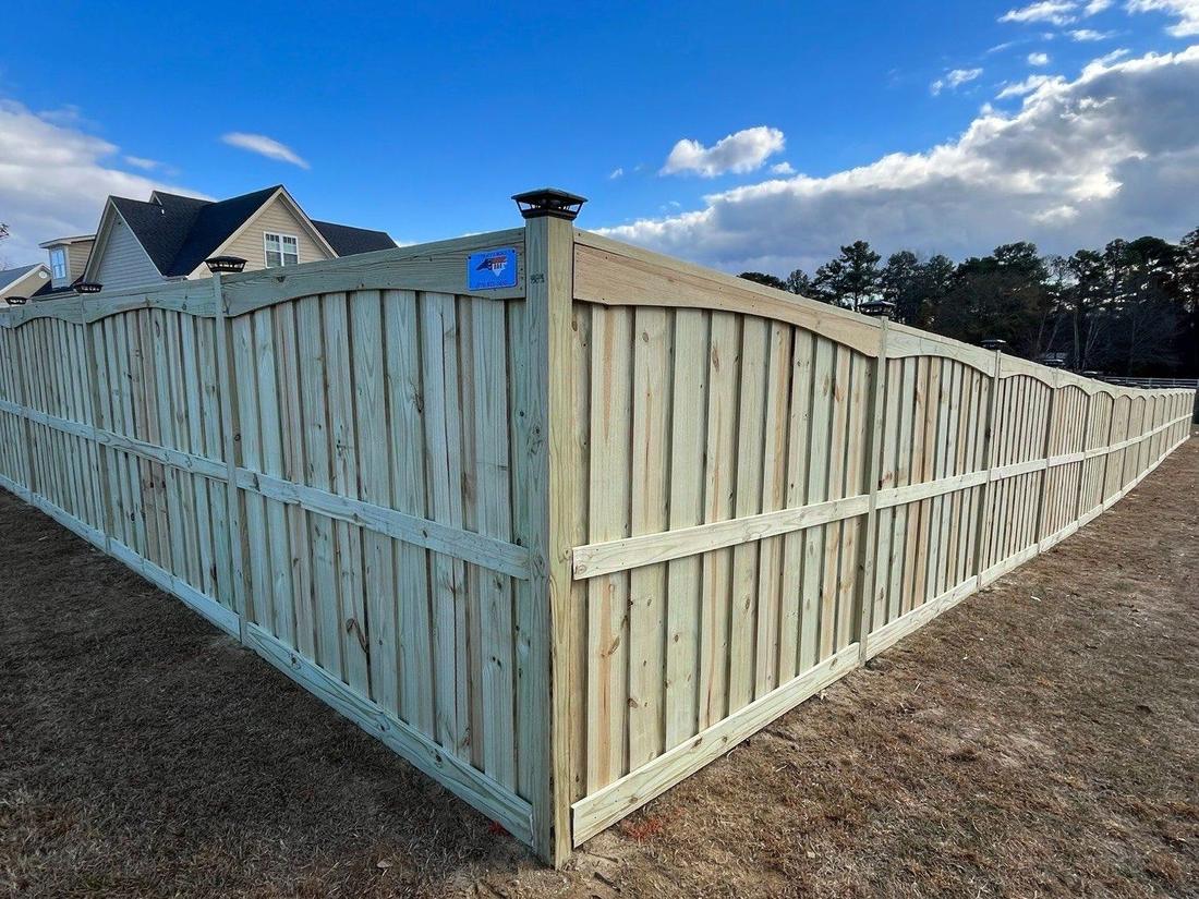 A new wood privacy fence with a scalloped top rail and post caps, running along a lawn between two houses.