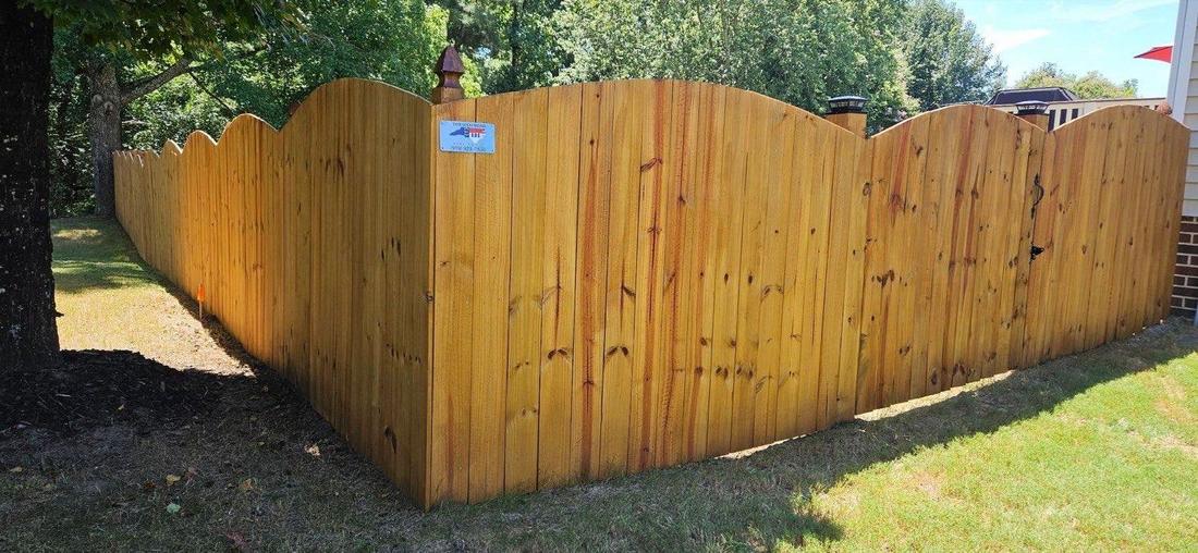 A honey-stained wood fence with a scalloped top, turning a corner around a mulched bed.