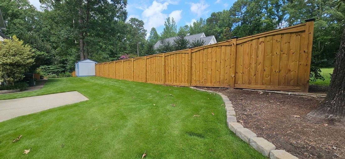 A stained wood fence running the length of a mown lawn past a garden shed.
